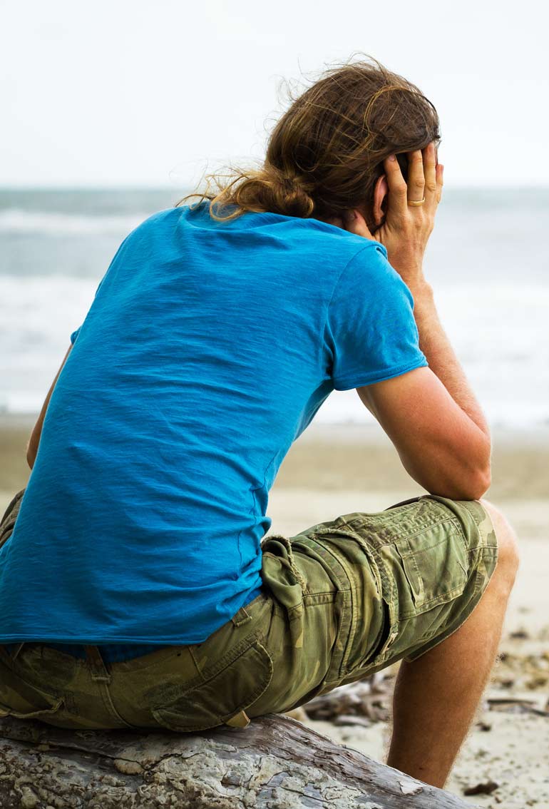 sad young man sitting by the beach