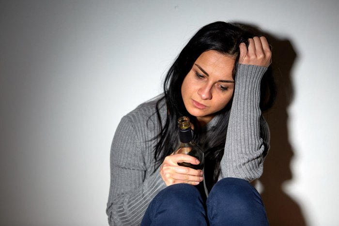 sad woman holding liquor bottle - alcohol use disorder
