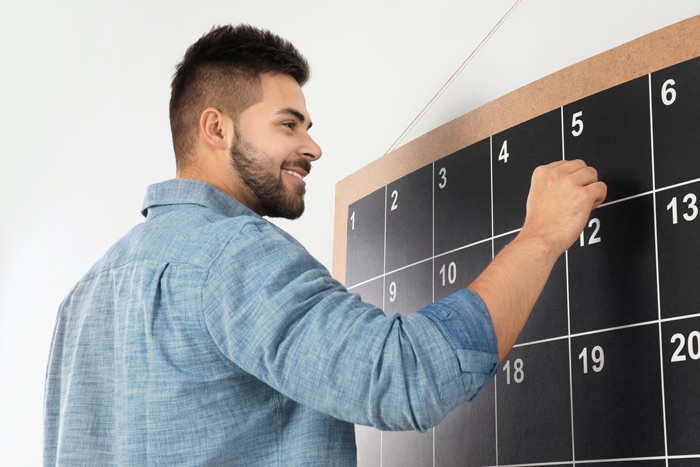 smiling man using large blackboard calendar to plan - routine