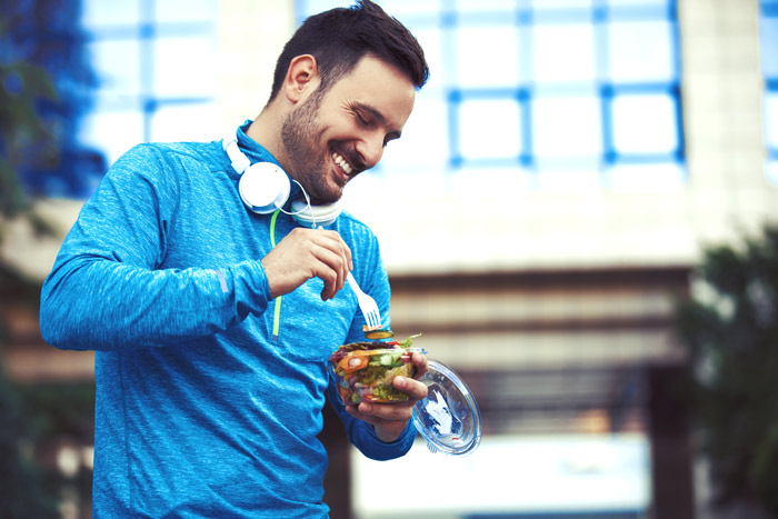 smiling man in blue exercise shirt eating bowl of fruit outdoors after exercising - immune system