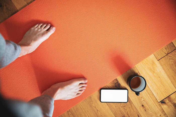 shot looking down at man's feet on orange yoga mat with coffee and cell phone nearby - rituals