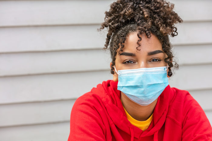 beautiful young Black woman in a red hoodie and disposable mask looking at camera - recovery during the pandemic