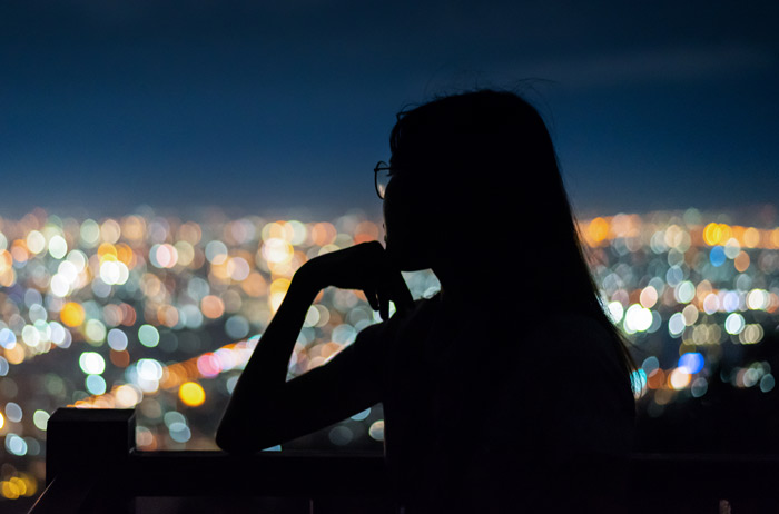 silhouette of young Asian woman looking out over city lights from balcony - addiction and suicide